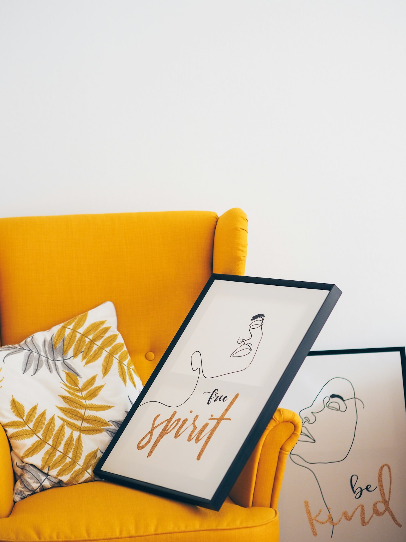 Framed prints with hand-lettered words on a mustard armchair